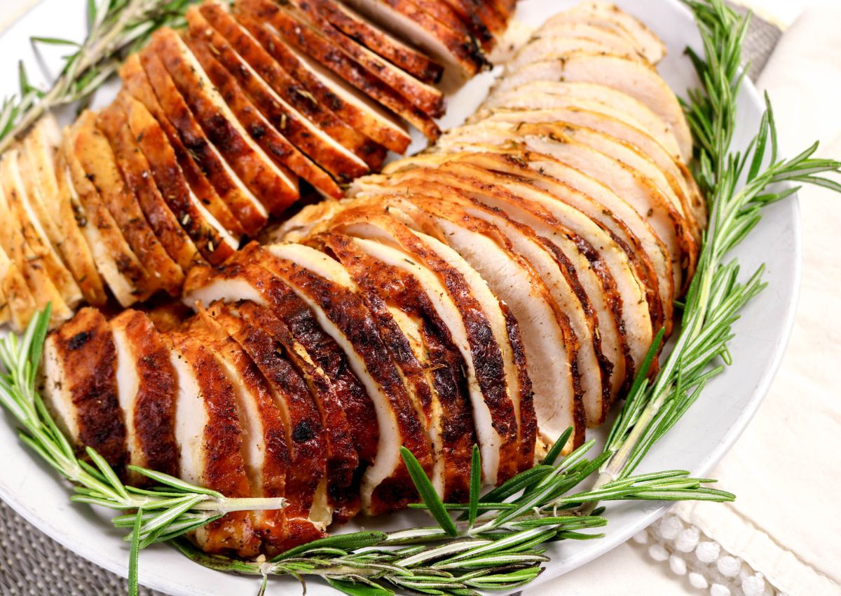 A plate of sliced roasted turkey breast arranged in rows, garnished with fresh rosemary sprigs.