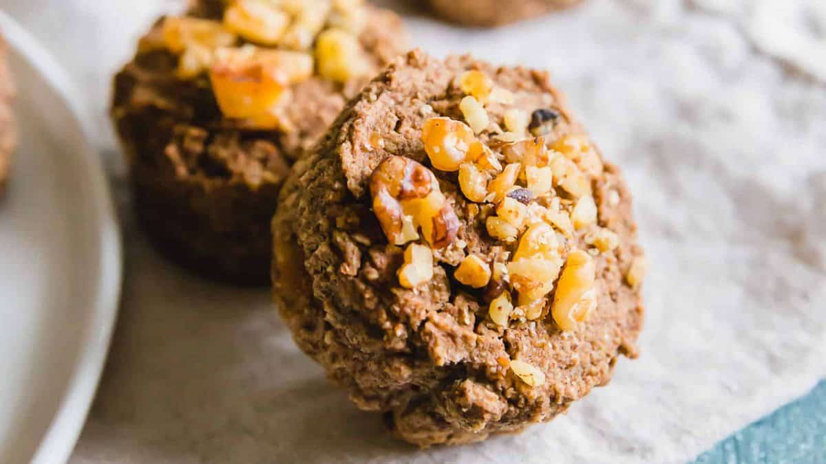 Close-up of two chocolate muffins topped with chopped walnuts on a light textured surface.