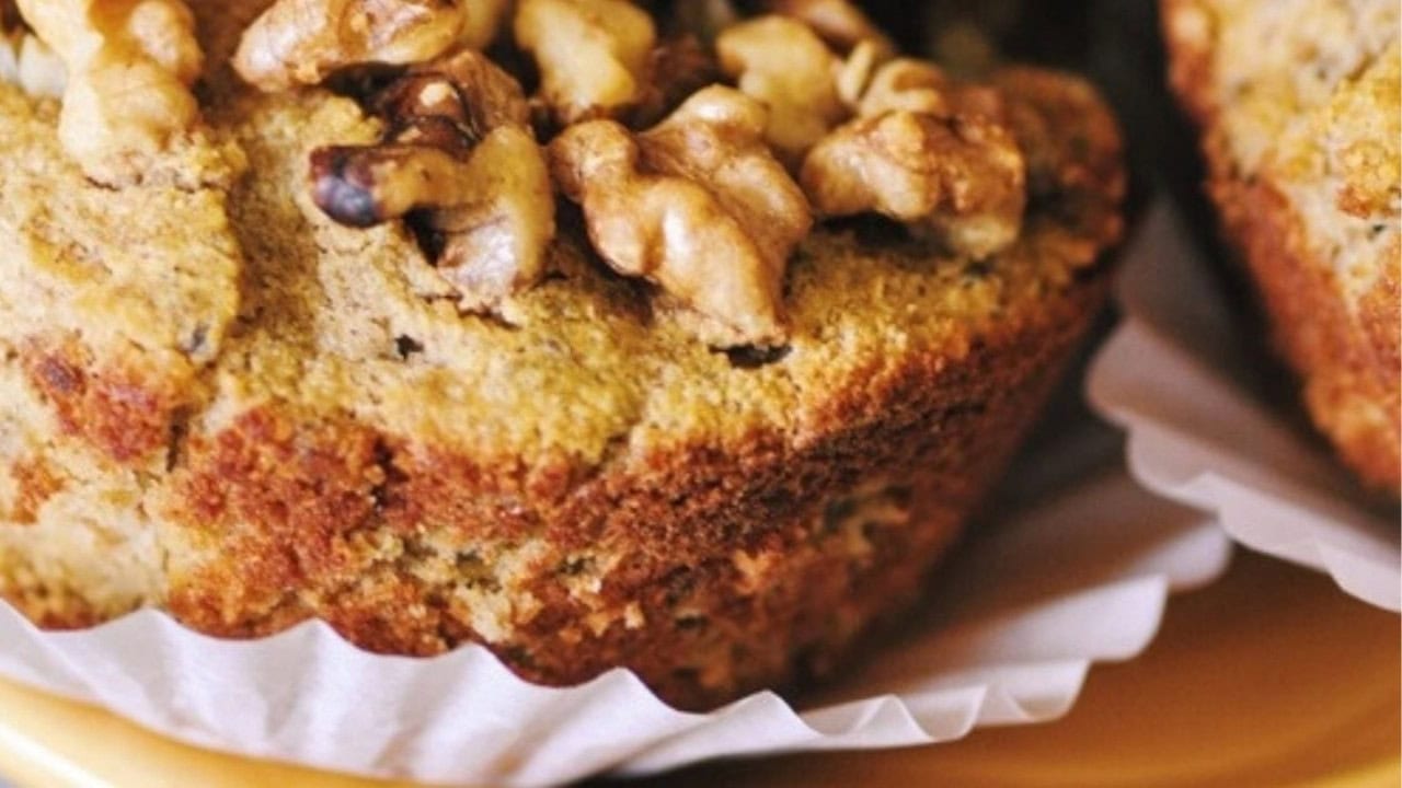 A close-up of a muffin topped with walnut pieces, sitting in a white paper liner.