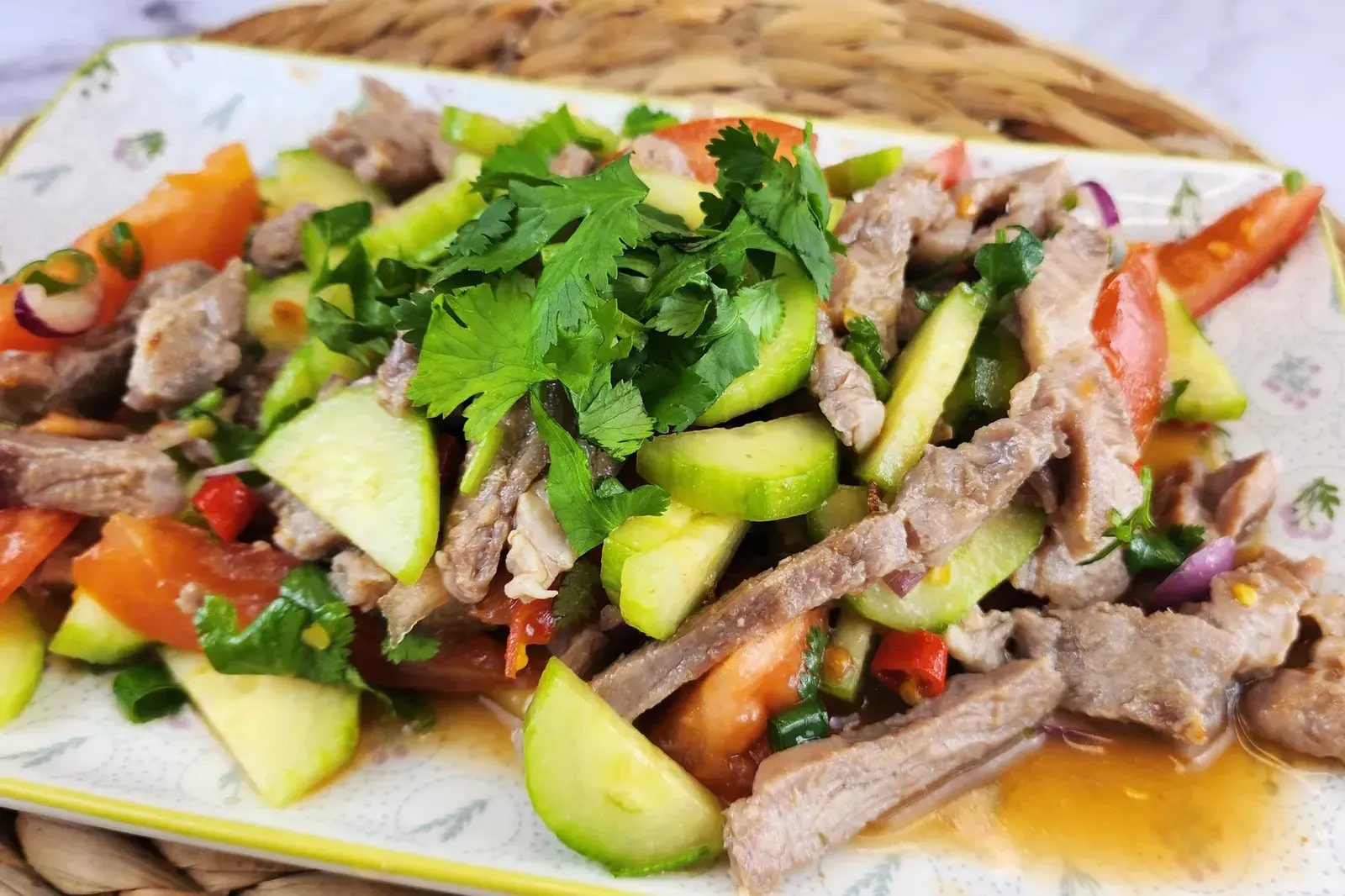 A plate of sliced beef mixed with cucumbers, tomatoes, red onions, and herbs, garnished with fresh cilantro on top.