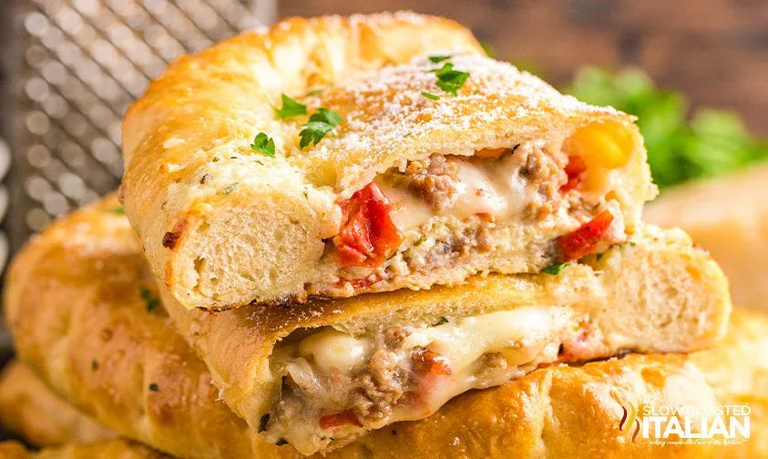 Two halves of a stuffed calzone filled with melted cheese, sausage, and red peppers, topped with parsley and grated cheese.