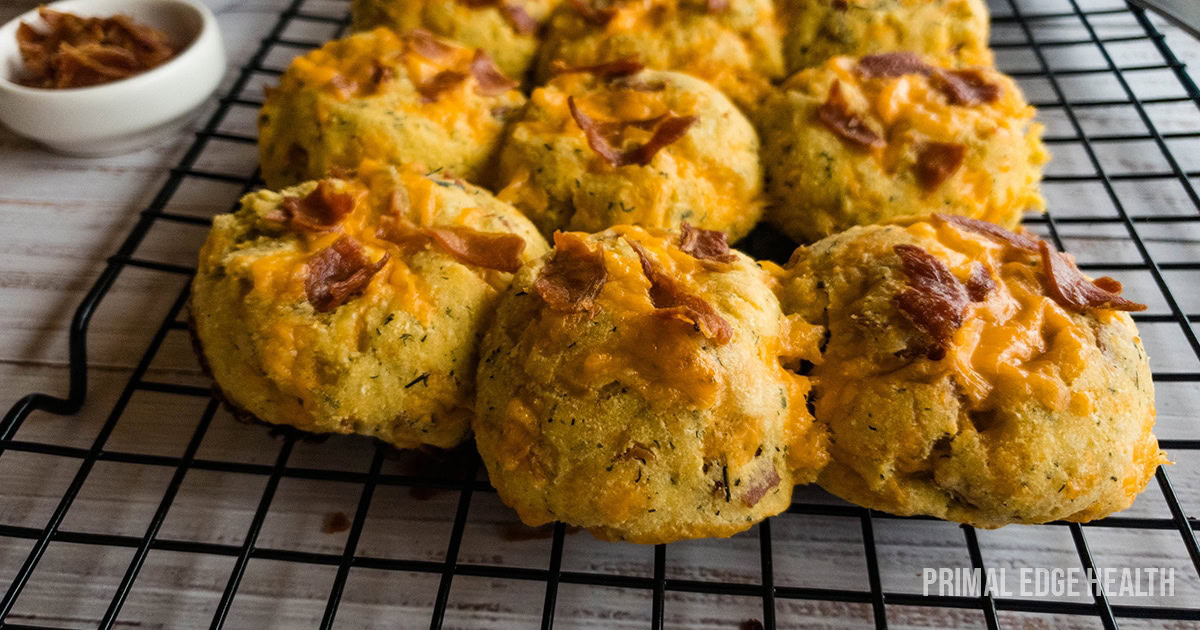 Nine cheesy biscuits topped with bacon bits cooling on a black wire rack, with a small dish of extra bacon bits in the background.