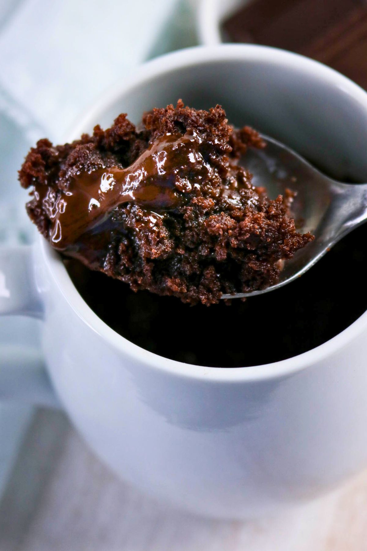 A spoon lifting a portion of chocolate mug cake with melted chocolate from a white mug.