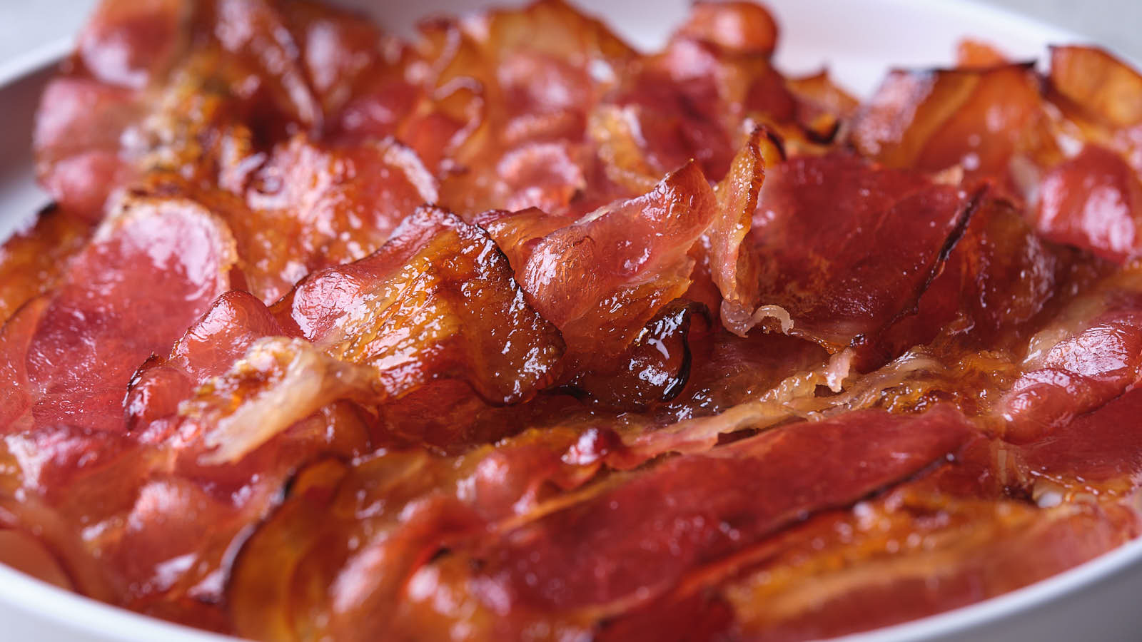 Close-up of several crispy, cooked bacon strips on a white plate.