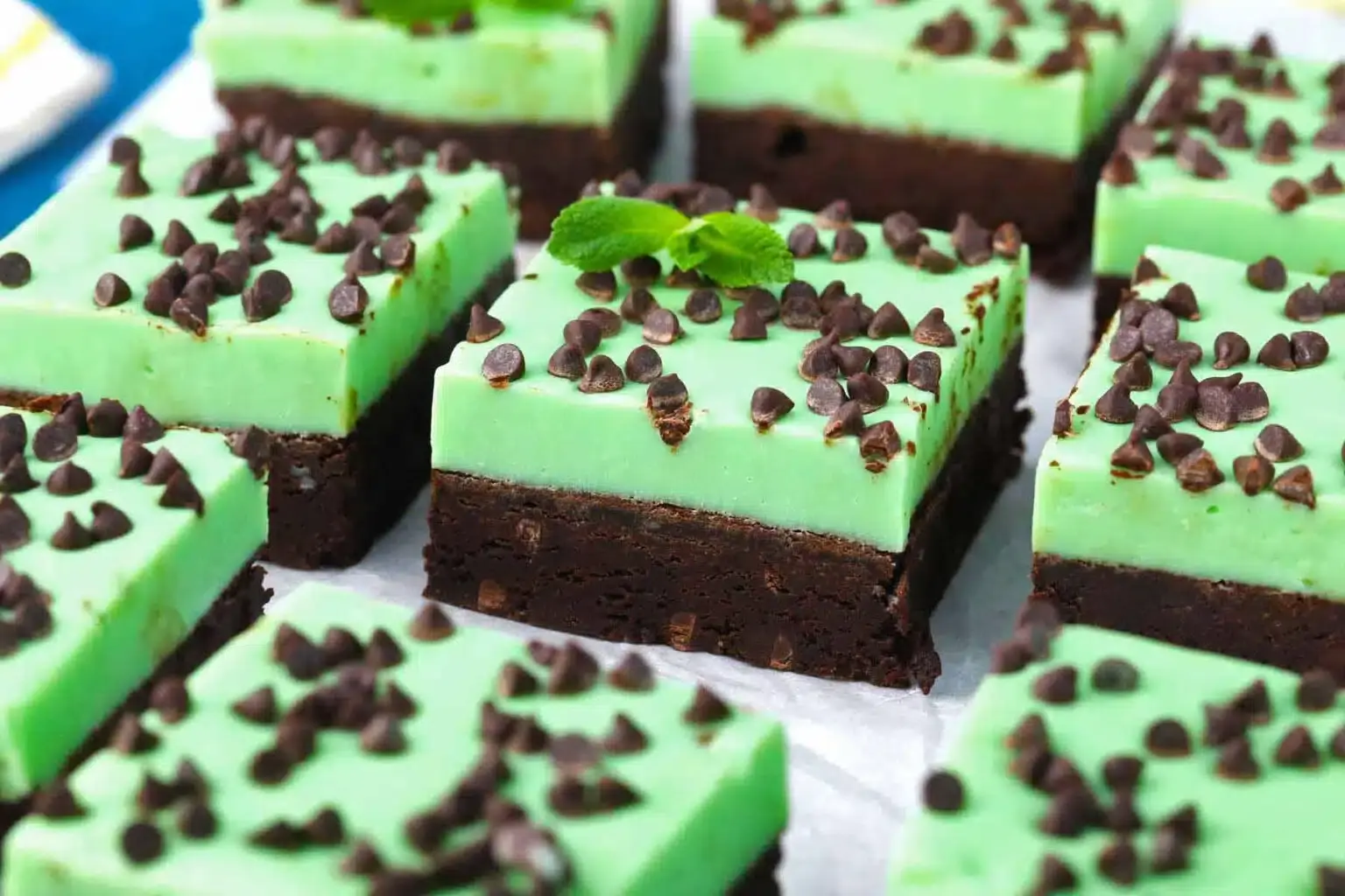 Squares of brownie with a thick mint green frosting layer and sprinkled with chocolate chips, arranged on parchment paper.