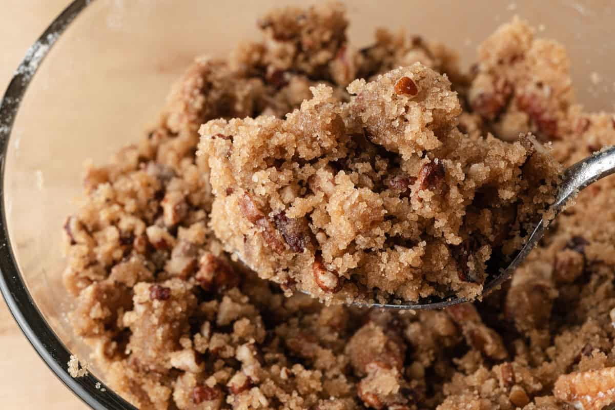 A close-up of a spoonful of crumbly pecan streusel mixture in a glass bowl.
