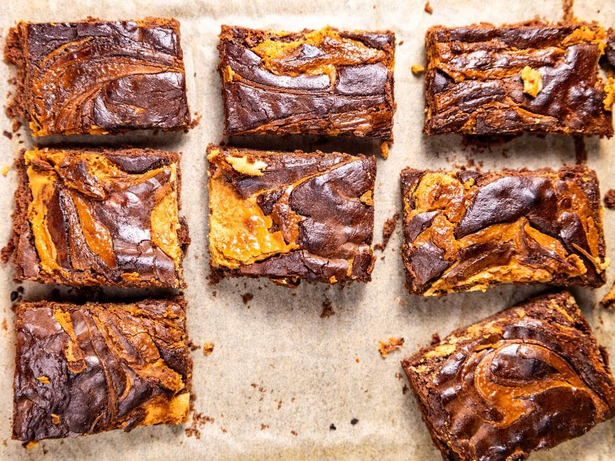 Nine square pieces of chocolate and peanut butter swirl brownies are arranged on parchment paper in a grid pattern.