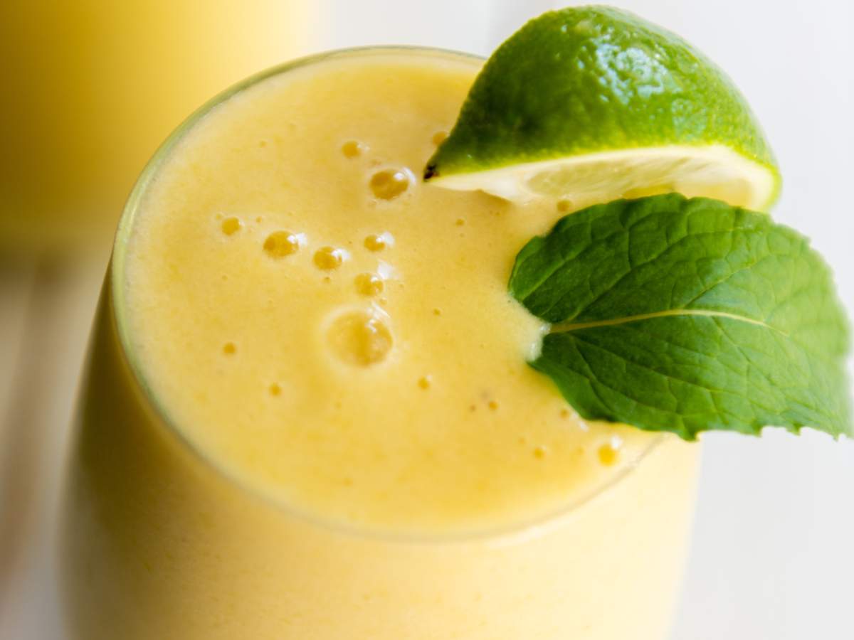 A glass of yellow smoothie topped with a lime wedge and a fresh mint leaf.