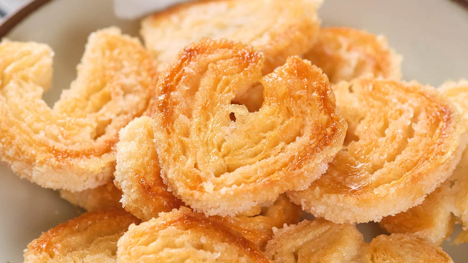 A plate of palmier cookies, also known as elephant ear pastries, with a golden, flaky, and sugar-coated appearance.