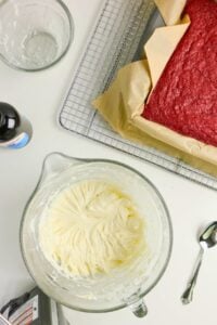 A red velvet cake and a glass bowl of frosting.