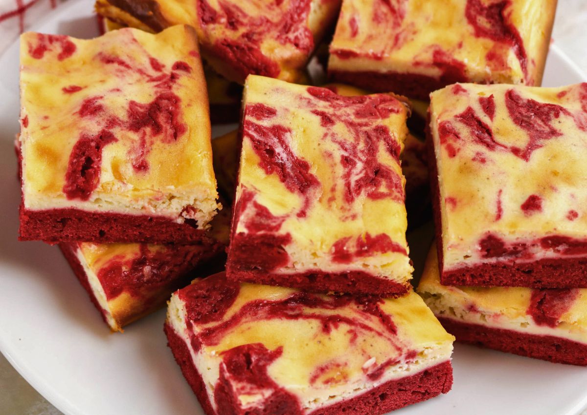 A plate of red velvet cheesecake bars with a marbled red and cream pattern on top.