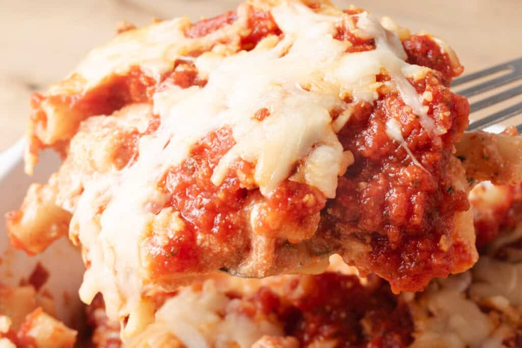 A close-up of a cheesy baked pasta dish with tomato sauce and melted cheese being lifted with a fork.