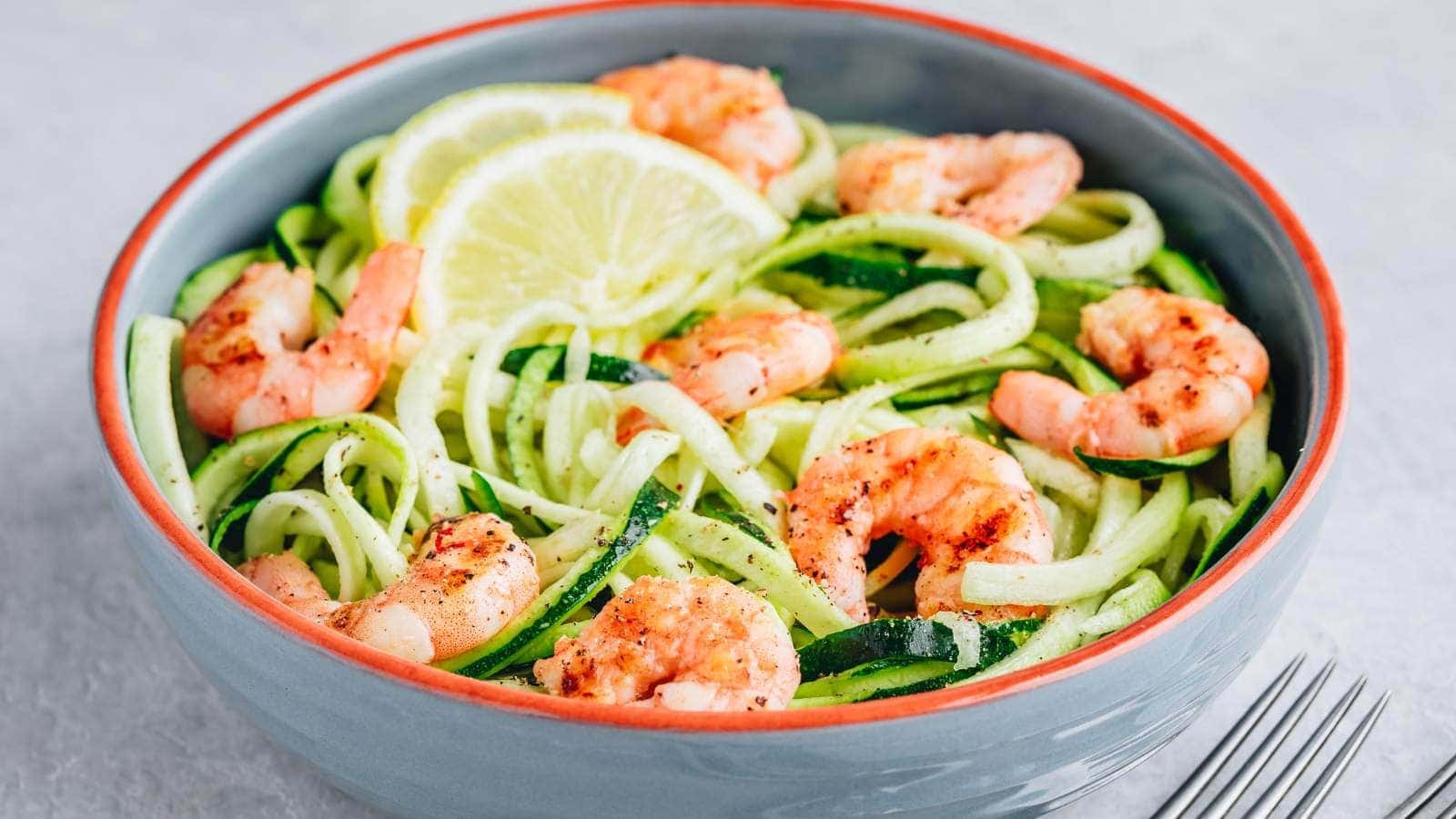 A bowl of zucchini noodles topped with cooked shrimp and garnished with two lemon slices.