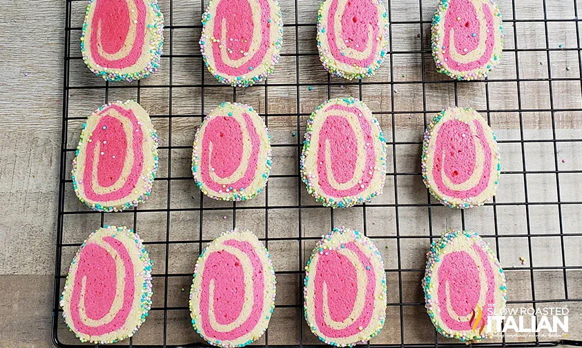Rectangular slice-and-bake cookies with pink and white swirls and sprinkled edges, cooling on a black wire rack.