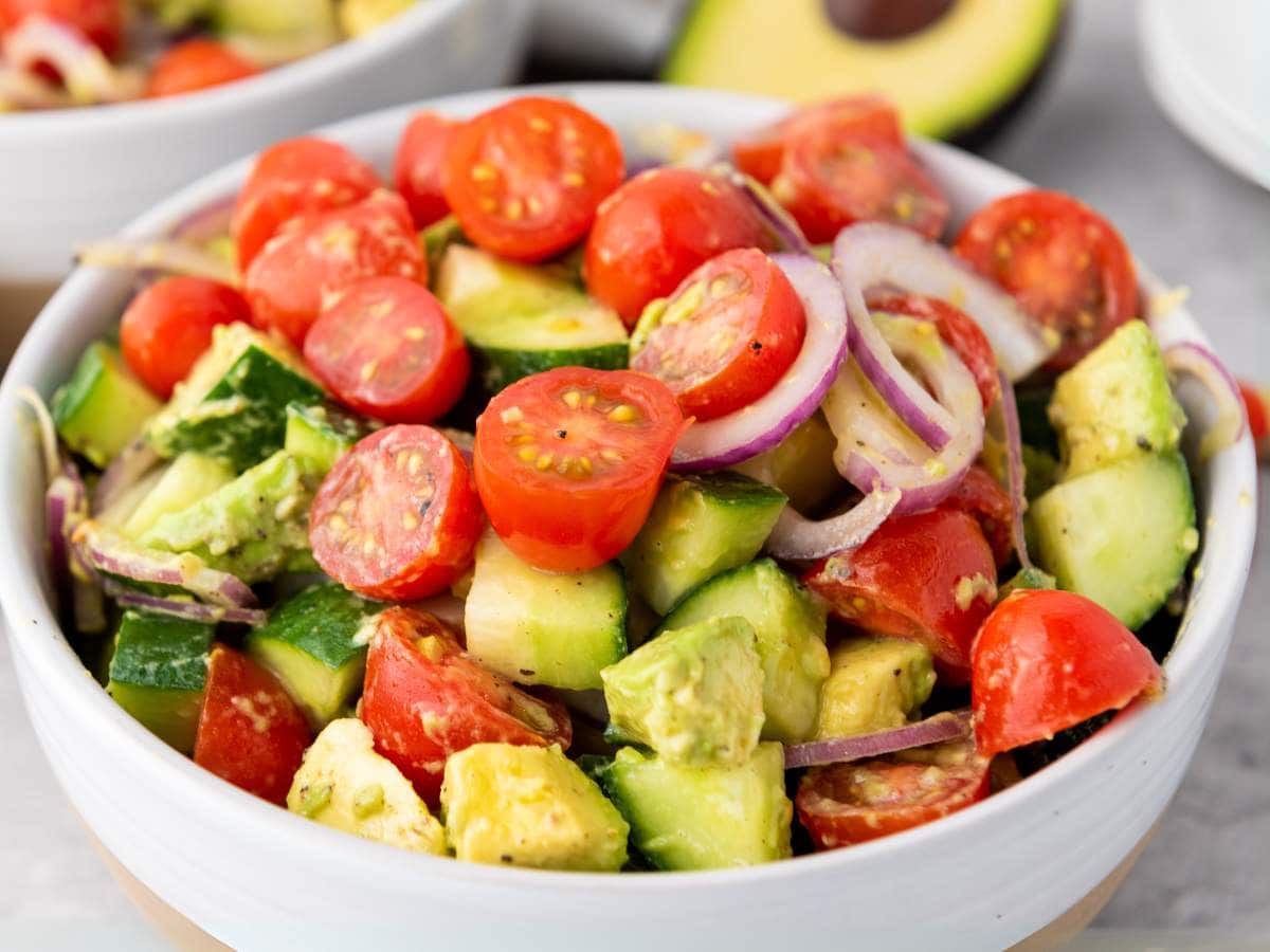 A bowl of salad containing cherry tomatoes, cucumber, avocado, and red onion slices.