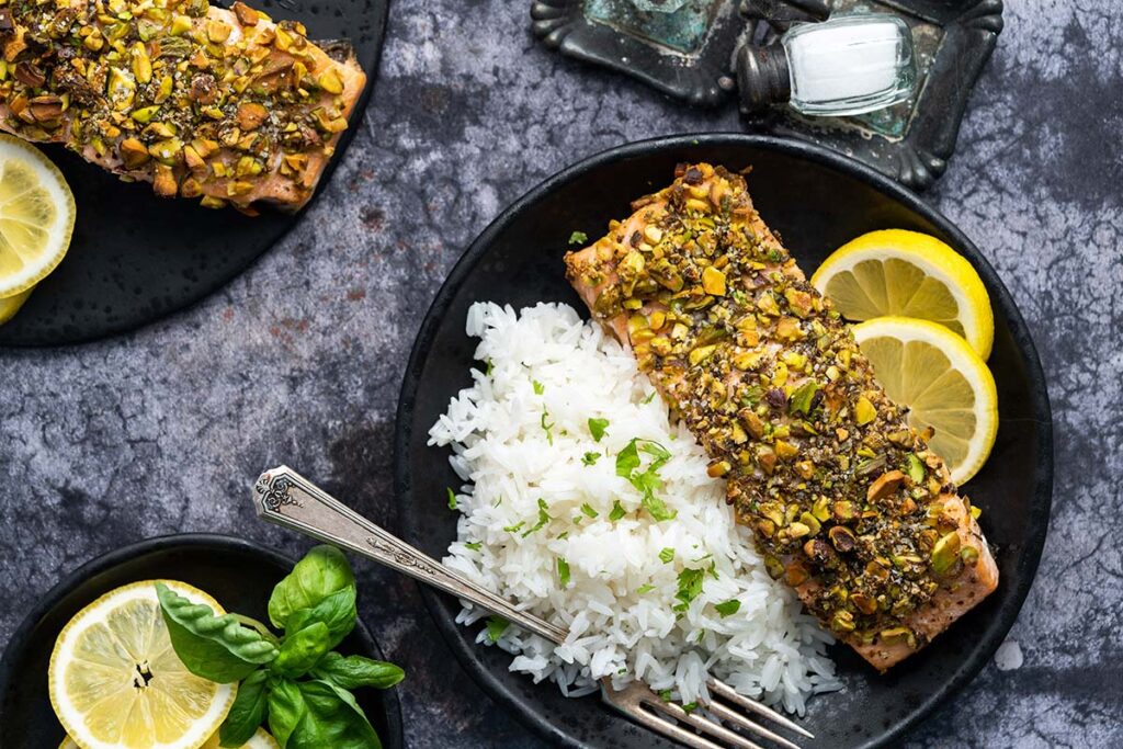 A plate with white rice, lemon slices, and a piece of salmon topped with chopped pistachios, photographed from above.