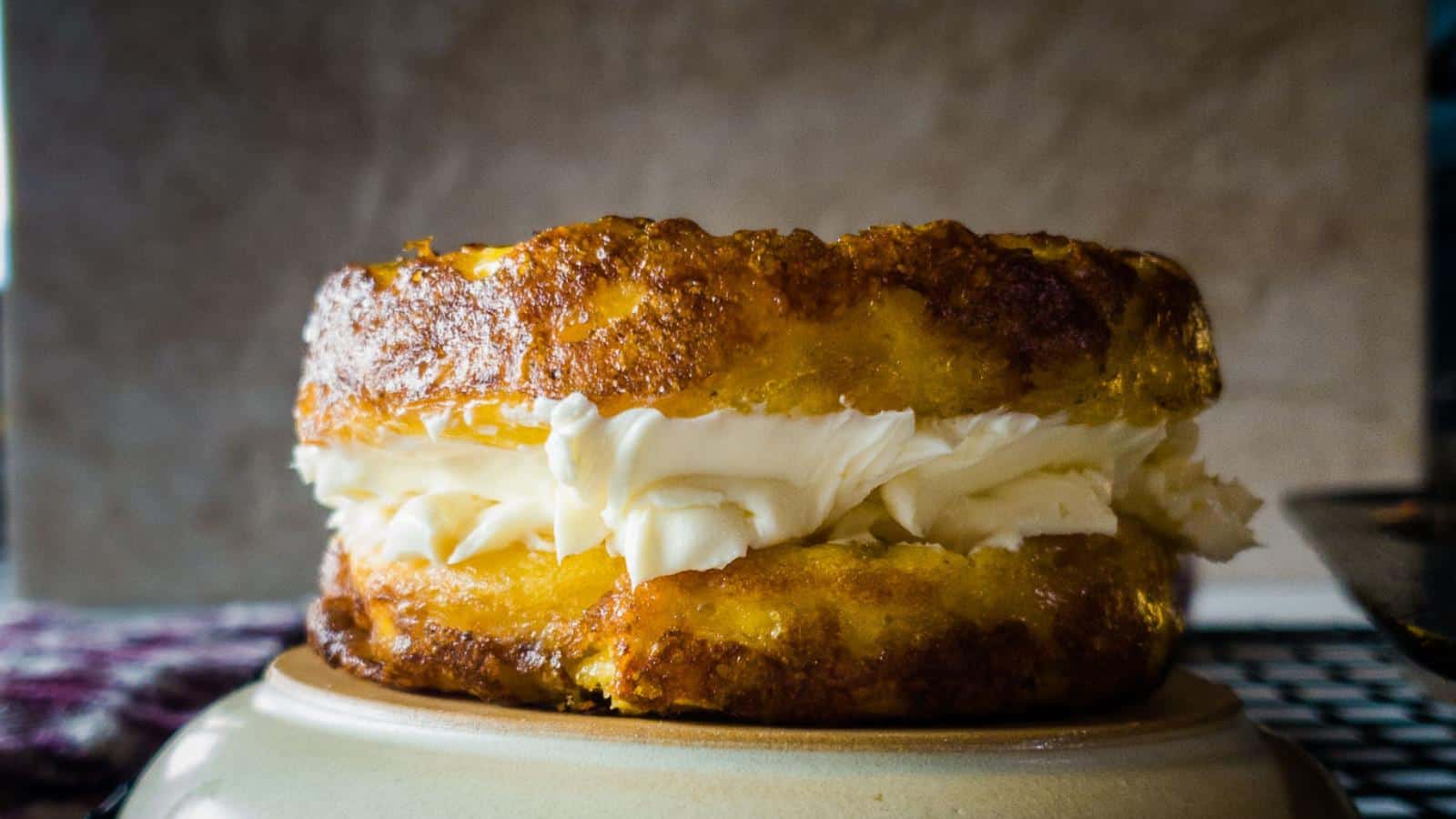 A close-up of a round sponge cake with a layer of cream filling in the middle, placed on a beige surface.