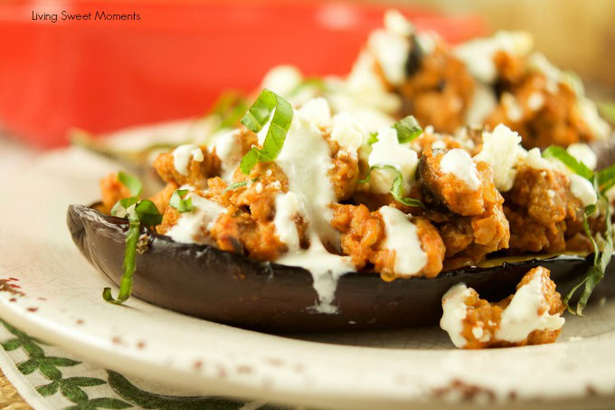 Close-up of a stuffed eggplant topped with a tomato-based meat mixture, fresh basil, and a drizzle of white sauce on a plate.