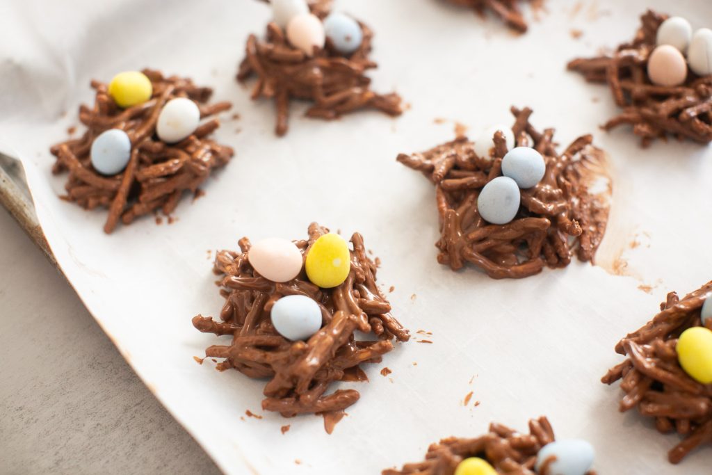 Clusters of chocolate-covered pretzel sticks topped with pastel candy eggs arranged on parchment paper.