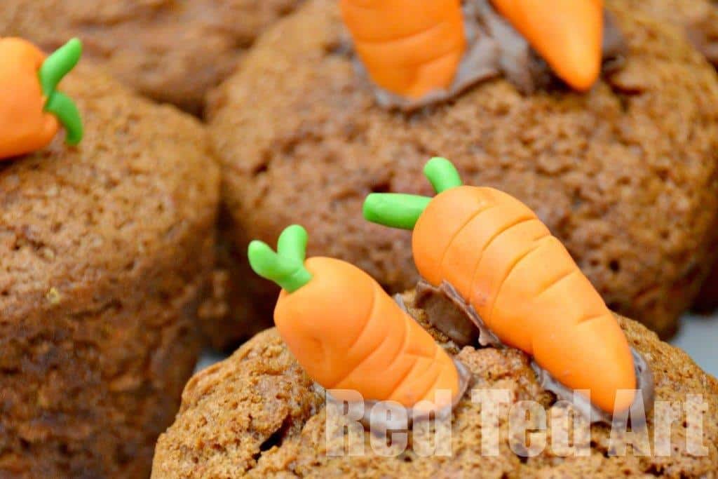 Close-up of brown cupcakes topped with small decorative carrots made from orange and green fondant.