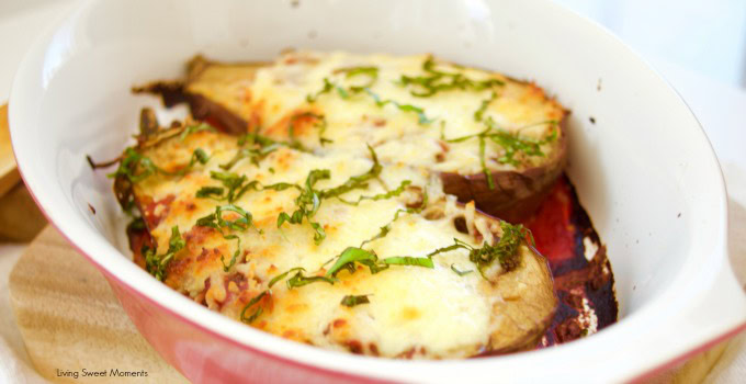 Baked eggplant halves topped with melted cheese and fresh herbs in a white baking dish.