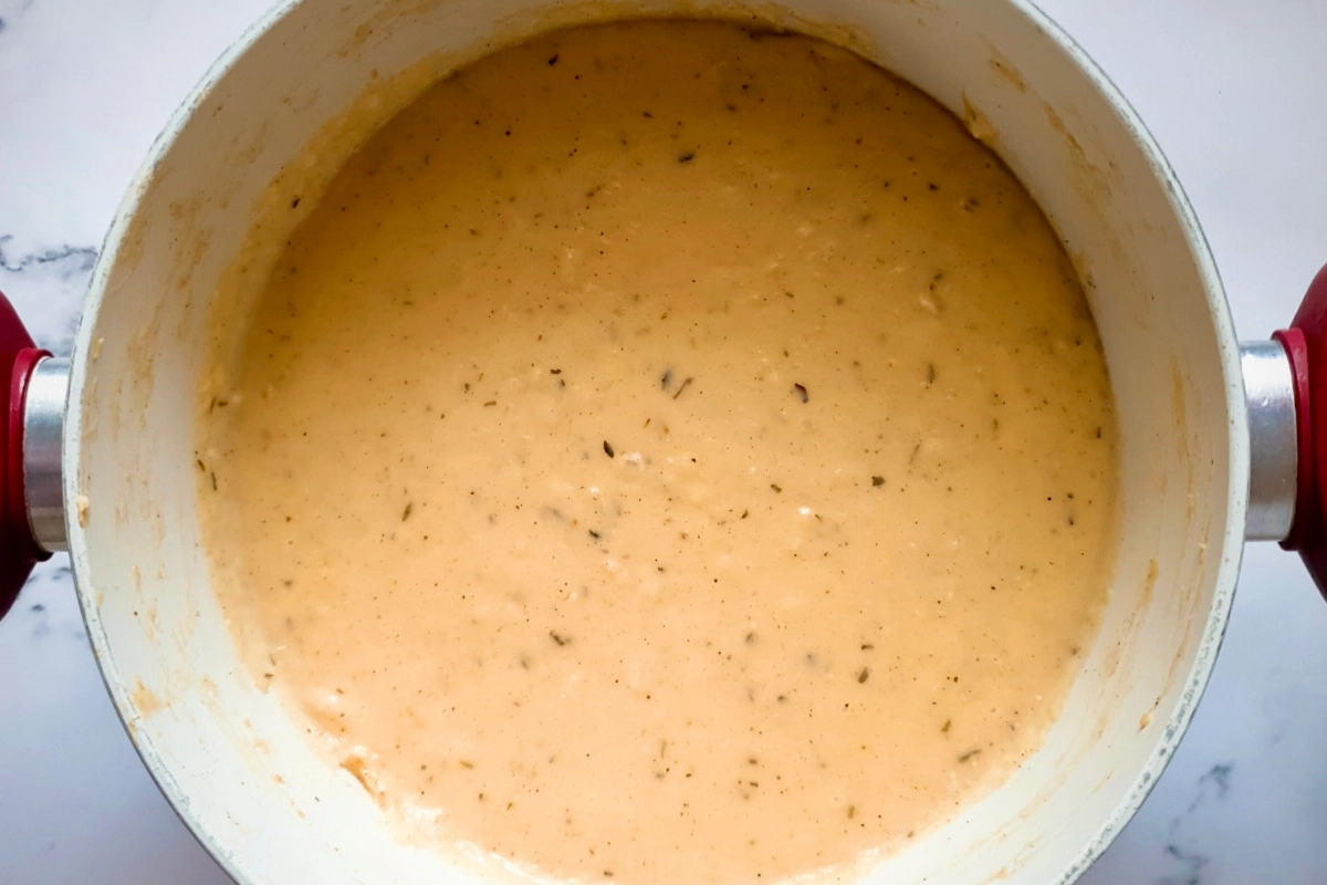A pot filled with creamy, orange-colored soup or sauce speckled with herbs, viewed from above.