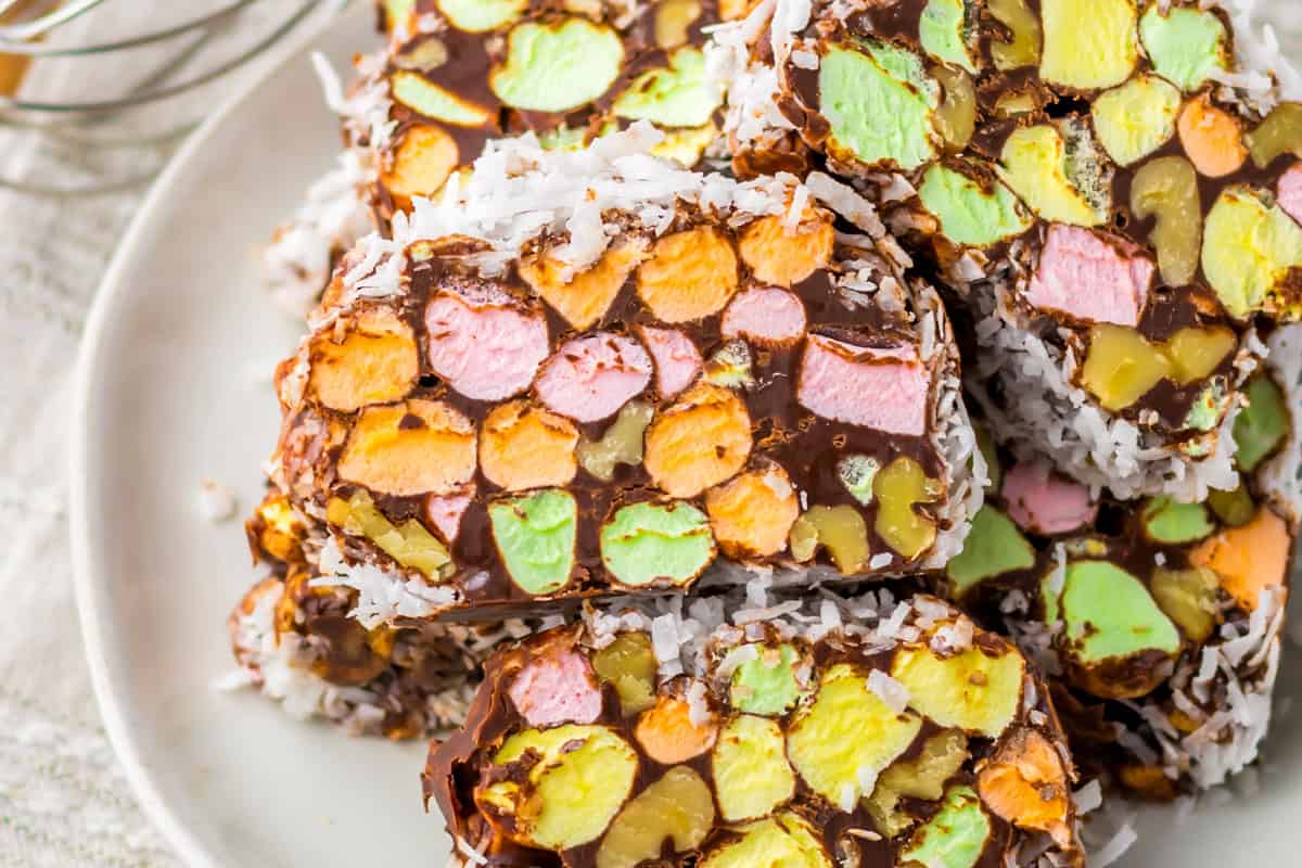 Slices of dessert made with colorful mini marshmallows, chocolate, walnuts, and shredded coconut arranged on a white plate.