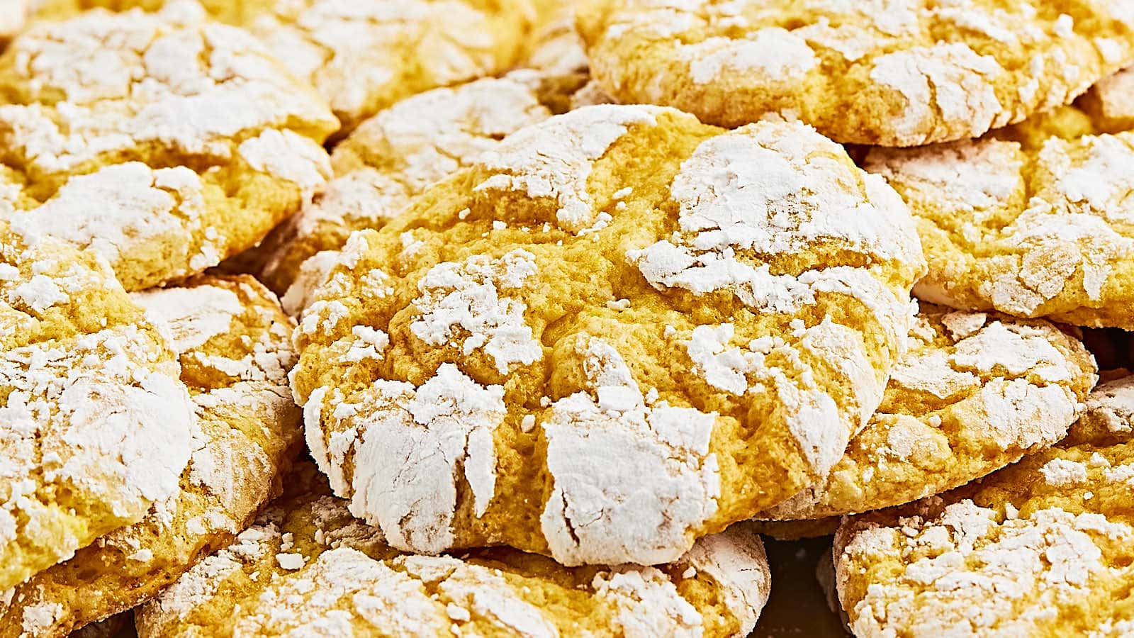 A close-up view of several yellow cookies with a cracked surface, dusted with powdered sugar.