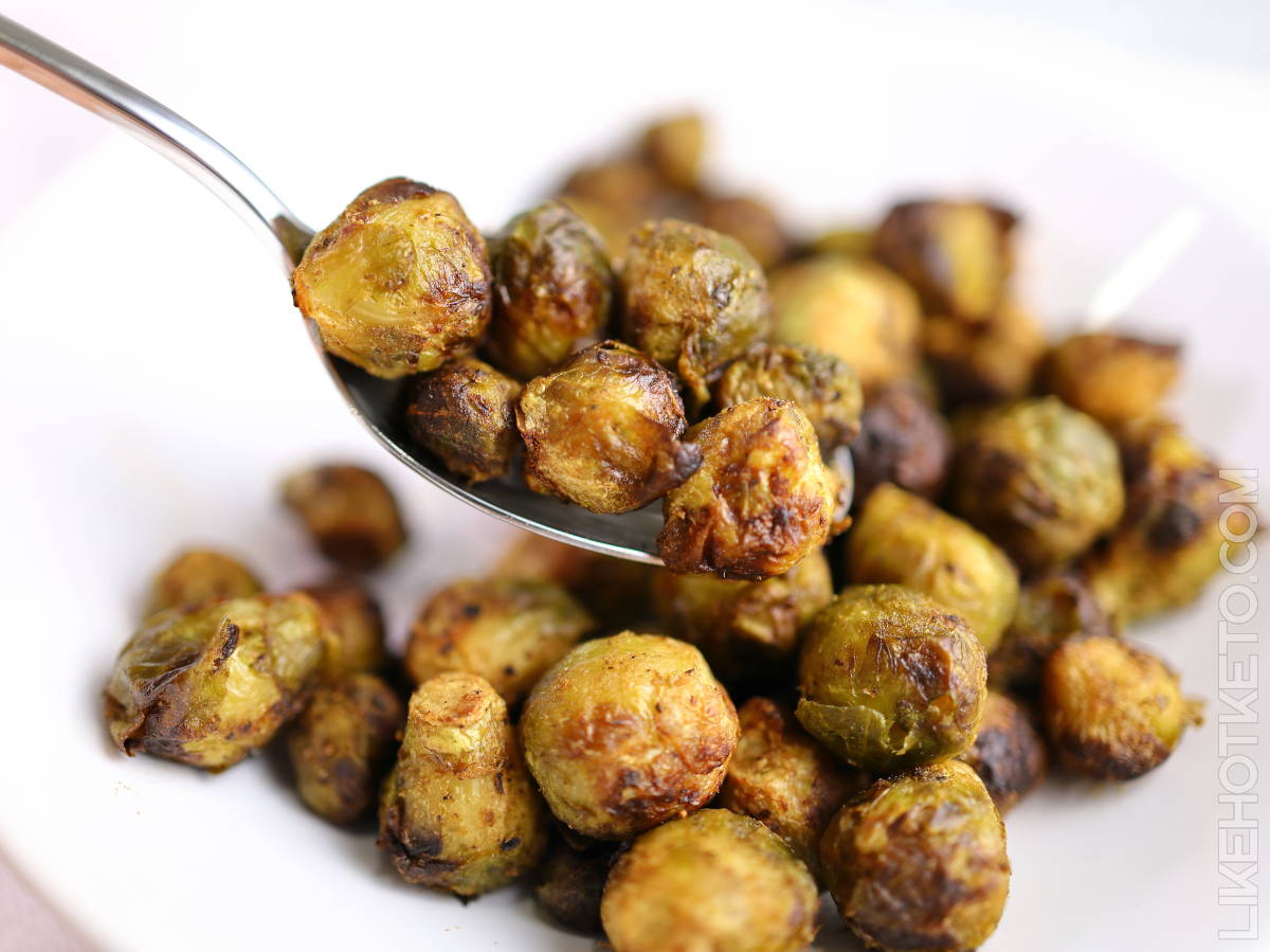 A close-up of roasted Brussels sprouts on a white plate, with a spoon lifting several pieces.