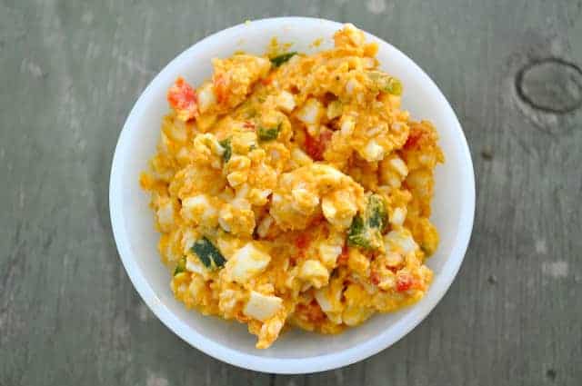 A white bowl filled with scrambled eggs mixed with chopped vegetables, placed on a gray wooden surface.