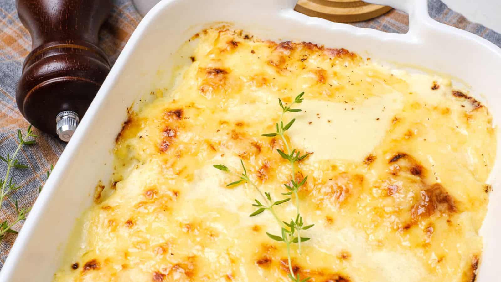 Baked potato gratin in a white dish, topped with melted cheese and garnished with fresh thyme sprigs.