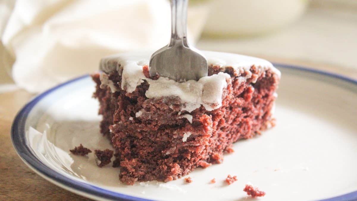 A fork is inserted into a slice of chocolate cake with white icing on a white plate with a blue rim.
