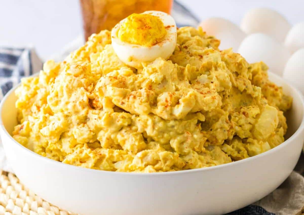 A bowl of classic yellow potato salad topped with half a hard-boiled egg and sprinkled with paprika.