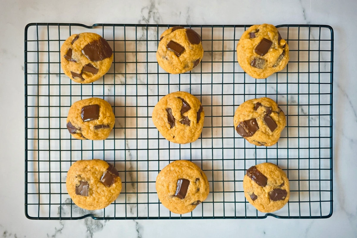 Nine chocolate chunk cookies cool on a black wire rack set on a white marble surface.