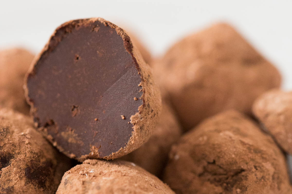 A close-up of chocolate truffles, with one truffle cut in half to show its smooth, dark interior and cocoa powder coating.