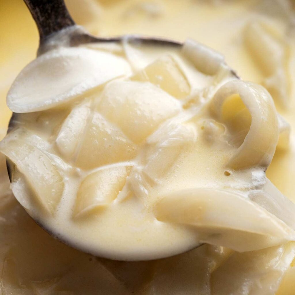 A close-up of a spoonful of creamed onions in a thick, creamy sauce.