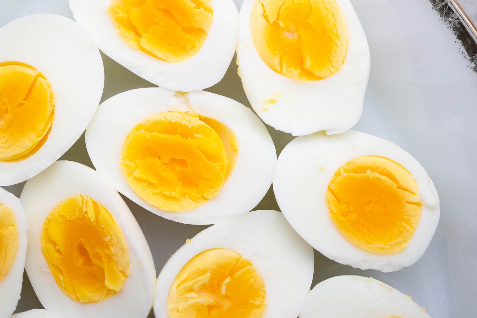 Several hard-boiled eggs cut in half lengthwise, showing firm whites and bright yellow yolks, arranged on a white surface.