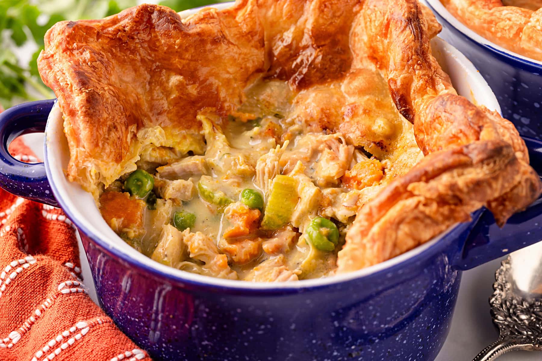 A blue ceramic bowl filled with chicken pot pie topped with a golden, flaky pastry crust, showing pieces of chicken, peas, carrots, and creamy sauce.