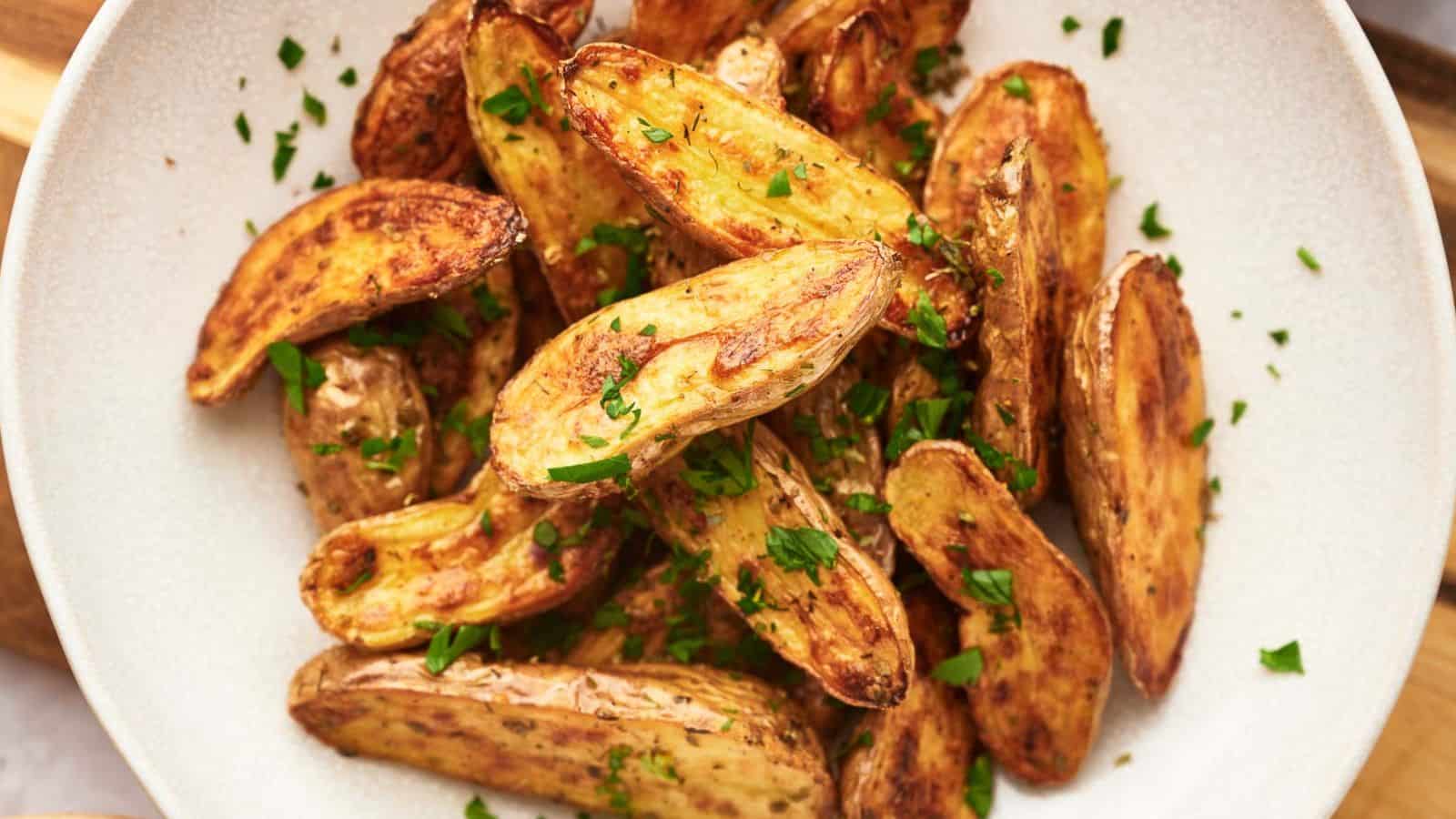 A white plate filled with roasted fingerling potatoes, garnished with chopped fresh parsley.