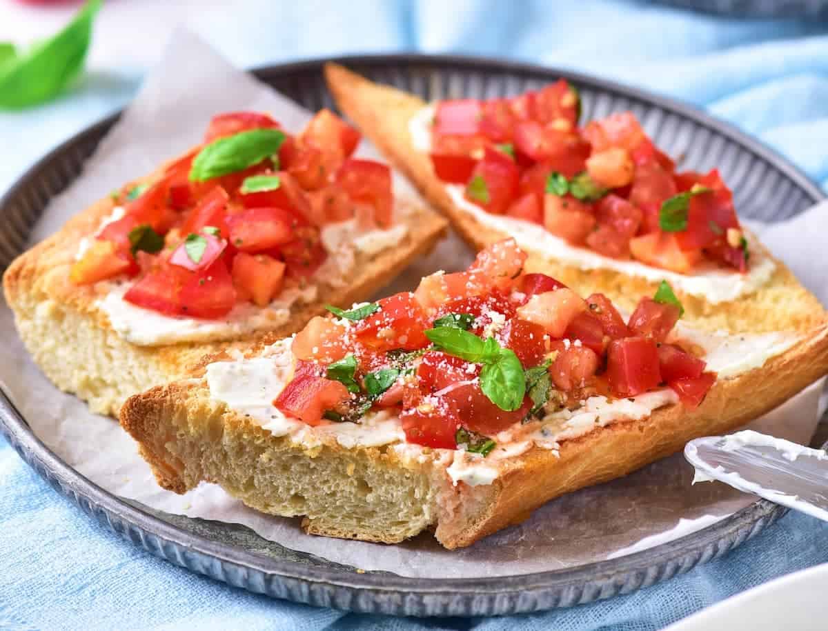 Three slices of toasted bread topped with chopped tomatoes, herbs, and a spread are arranged on a round plate lined with parchment paper.