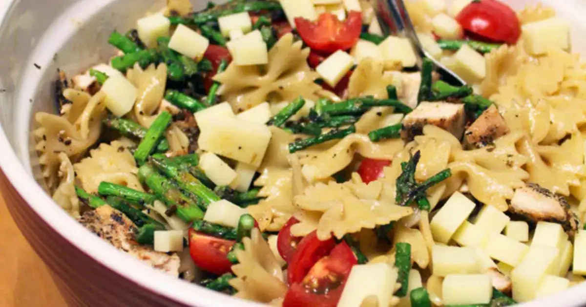 A bowl of farfalle pasta mixed with grilled chicken, asparagus, cherry tomatoes, and diced cheese.