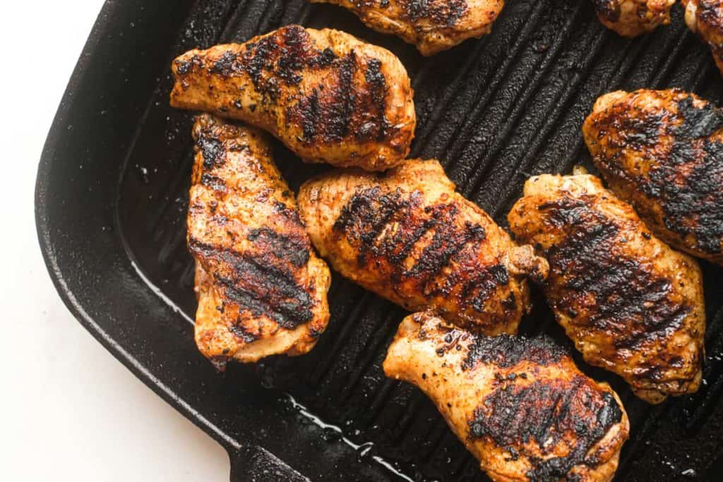 Grilled chicken pieces with visible char marks cooking on a black cast iron grill pan.