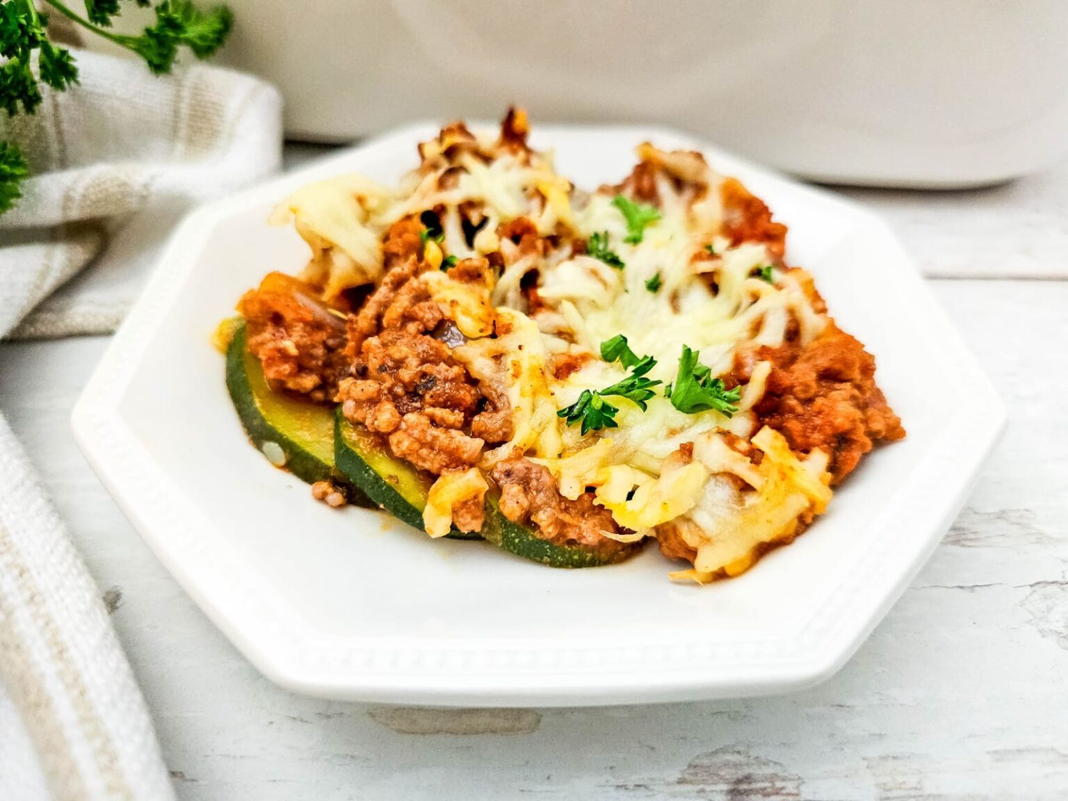 A serving of zucchini lasagna topped with melted cheese and parsley on a white plate.