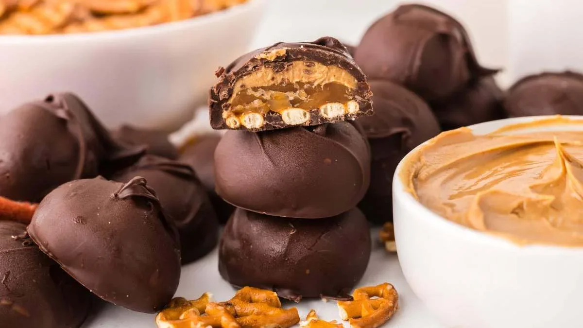 A stack of chocolate-covered pretzel and peanut butter truffles, with one cut open to show the filling; bowls of pretzels and peanut butter are nearby.