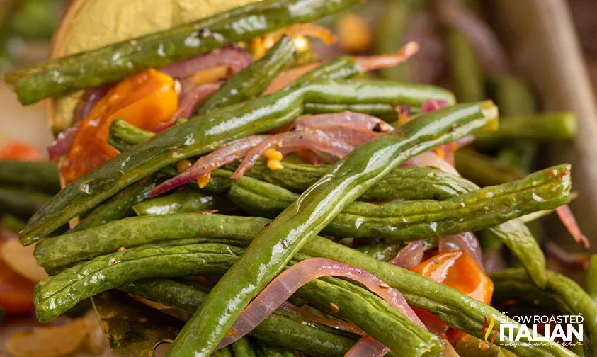 Close-up of sautéed green beans, sliced red onions, and bell peppers, lightly glazed, with The Slow Roasted Italian logo in the bottom right corner.