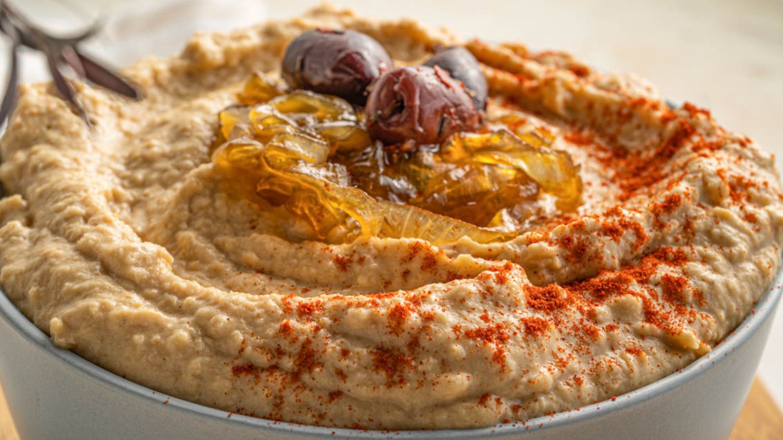 A bowl of hummus topped with caramelized onions, olives, and a sprinkle of paprika.