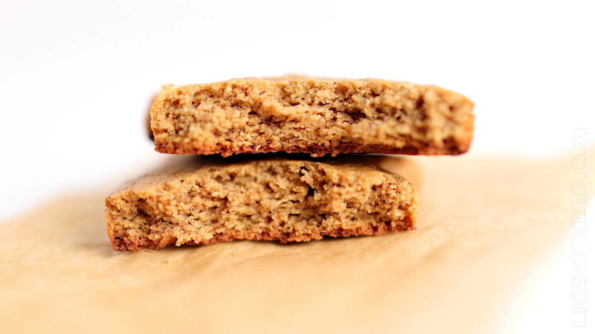 Two halves of a brown, crumbly cookie are stacked on a piece of brown parchment paper, showing their textured interior.