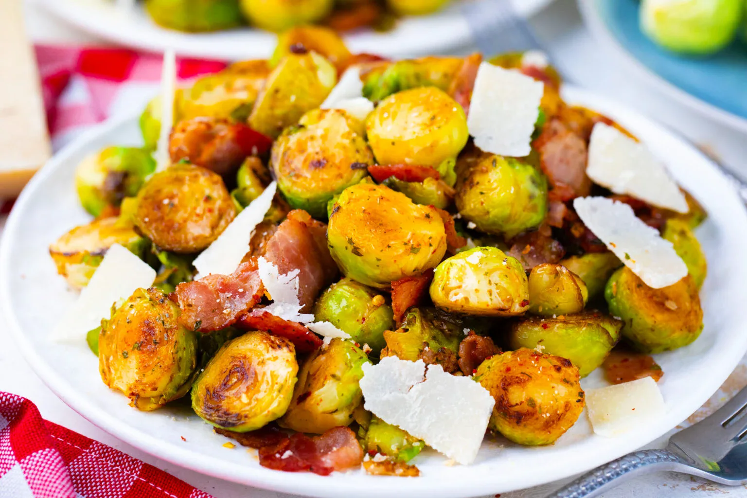 A plate of roasted Brussels sprouts mixed with bacon pieces and topped with shaved parmesan cheese.