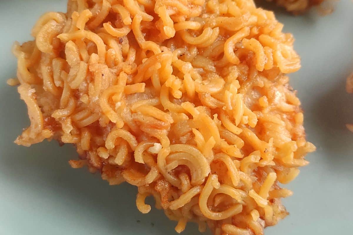 Close-up of a piece of food coated in cooked instant ramen noodles, showing a golden-brown, crispy texture.