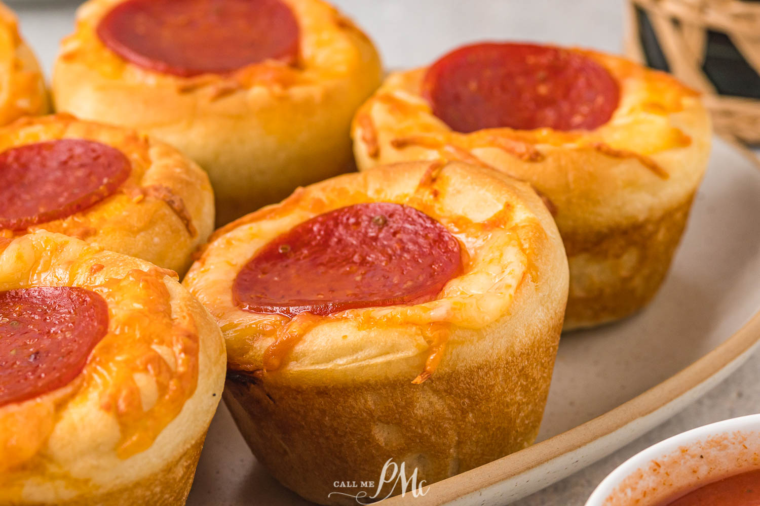 Close-up of pepperoni pizza muffins on a plate, each topped with melted cheese and a slice of pepperoni.